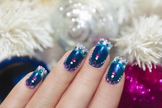 Winter blue manicure with snowflakes and pink triangular rhinestones near the white tree and colorful shiny balls